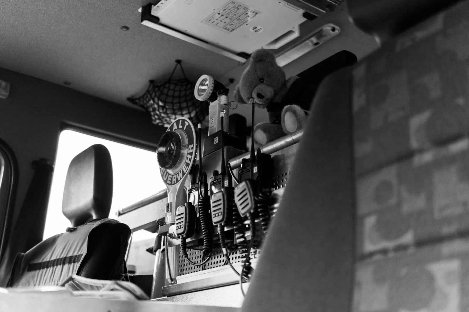 Black and white view inside emergency vehicle showing radios, seats, and a teddy bear.