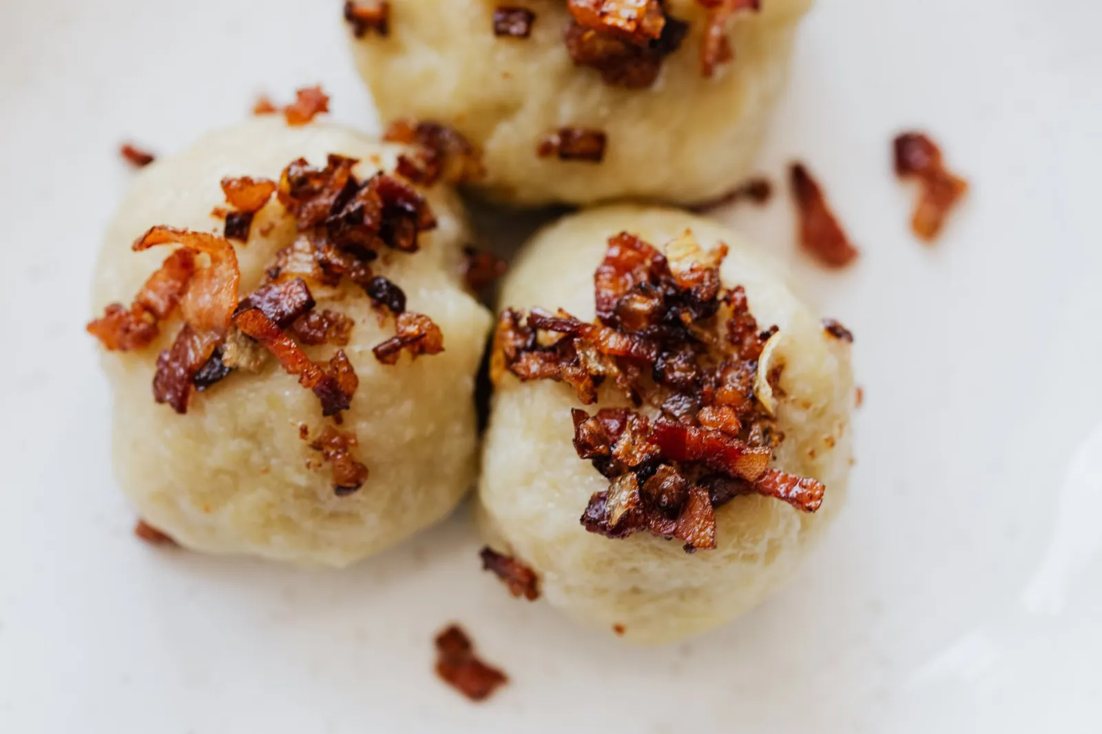 Top view closeup of yummy Polish pyzy made of potatoes and served with toasted bacon bits on ceramic plate