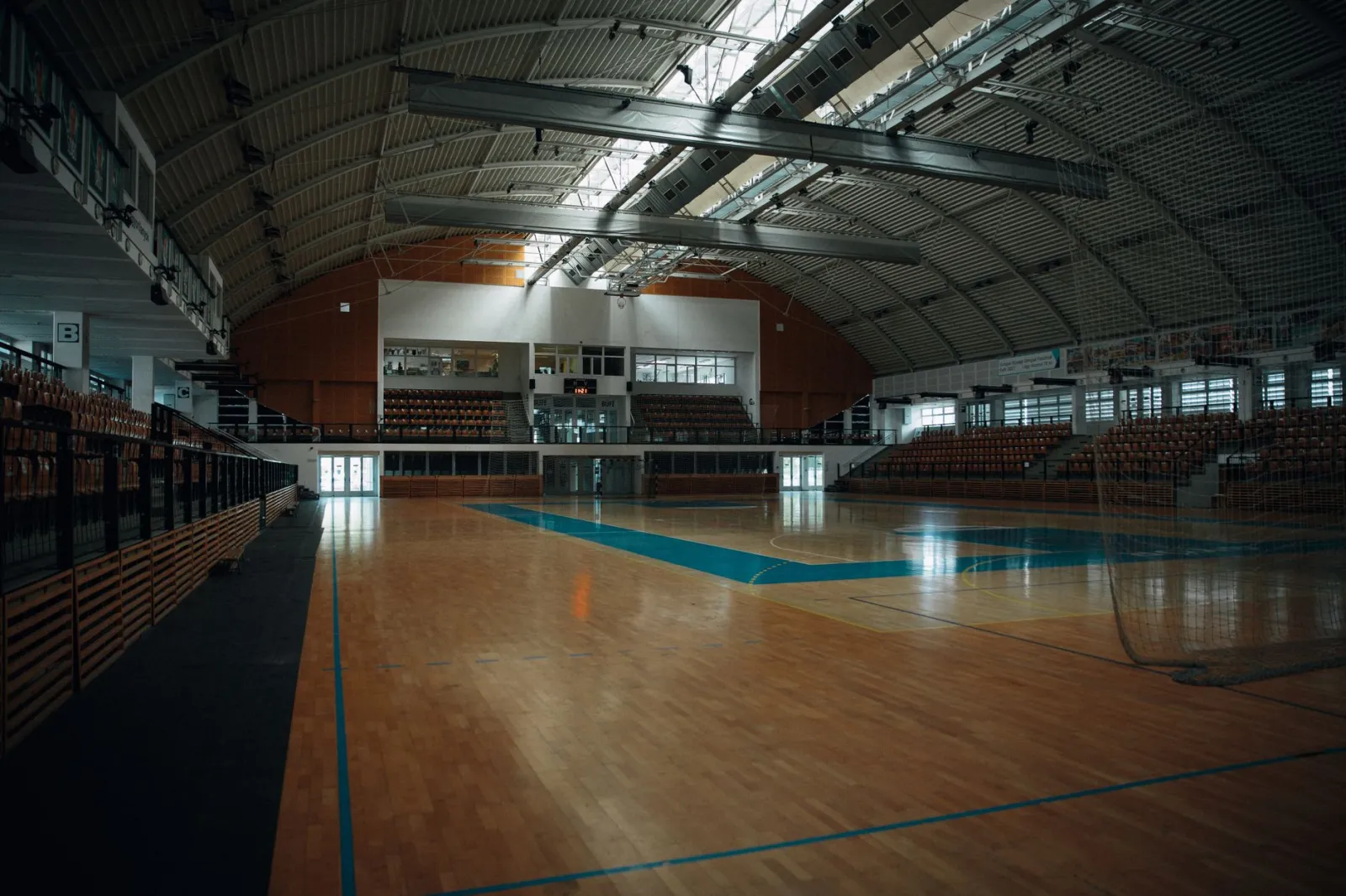 Empty indoor sports arena with hardwood flooring and bleachers, perfect for various sports activities.