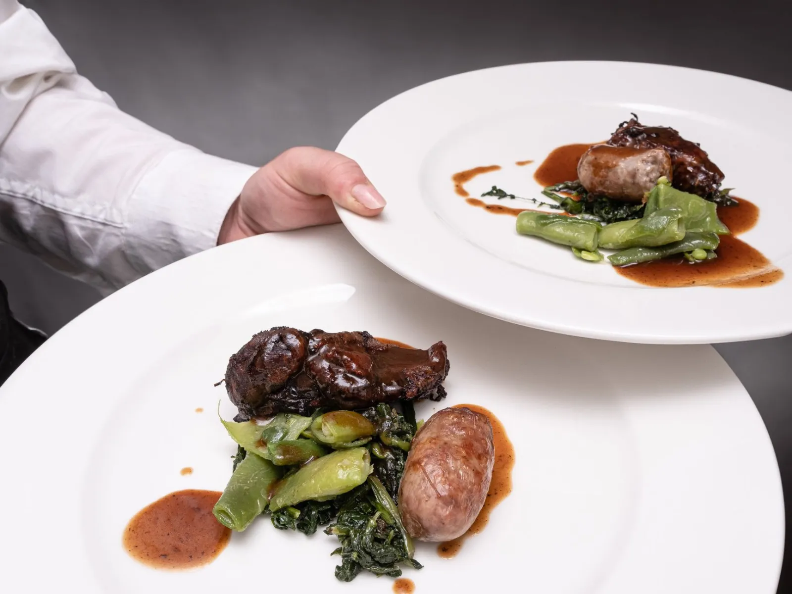 A chef elegantly serves gourmet plates with a savory dish of meat and vegetables.