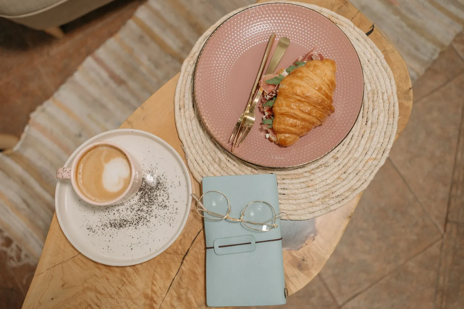 Enjoy a delicious brunch with a croissant sandwich and latte art coffee served on a cozy setup.